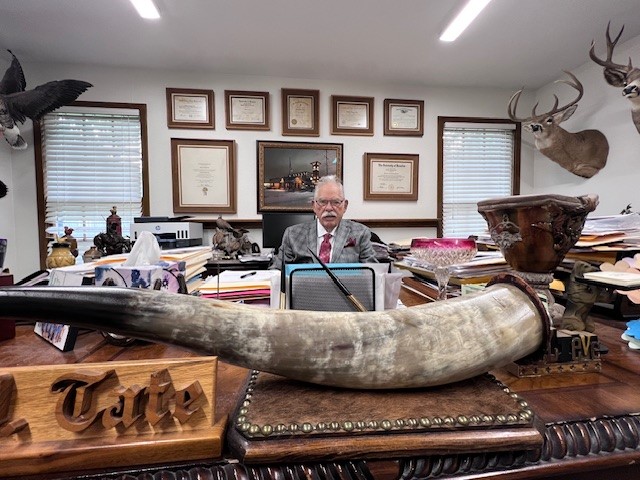 Grapevine Mayor William Tate sitting at his desk in an office filled with historic artifacts and awards.